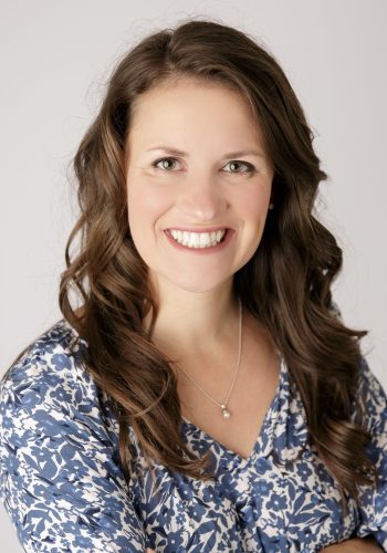 Close-up portrait of a smiling woman with long brown hair and a blue floral blouse.